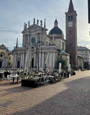 A historic building with a clock tower, outdoor seating with umbrellas, and a cobblestone plaza.
