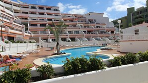 A hotel with a swimming pool surrounded by lounge chairs and palm trees. - Apartment with large terrace and beautiful pool view, solarium, private parking (Costa Adeje)