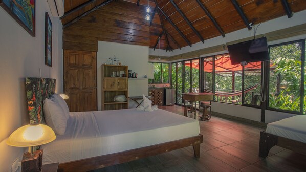 A bedroom with a bed, a desk, a chair, a wardrobe, and a window with a view of greenery. - Boca Tapada Lodge (Pital)