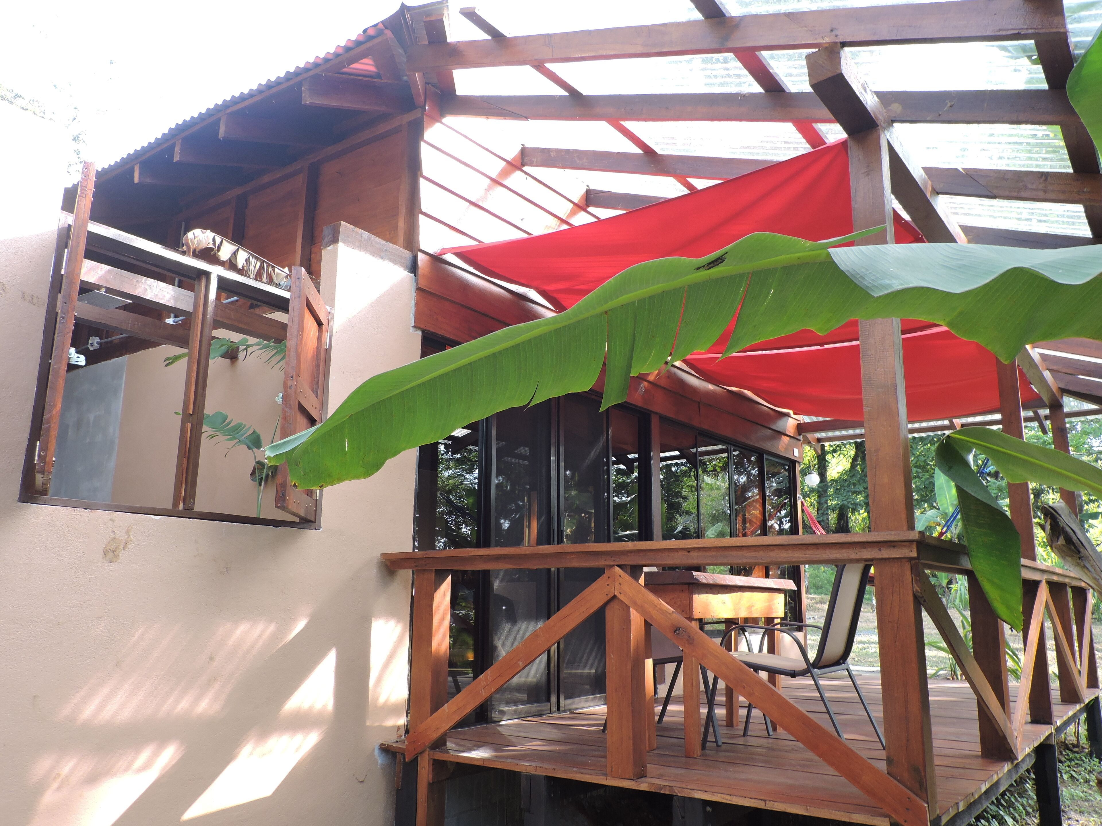 A wooden deck with a red canopy, a table, and chairs.