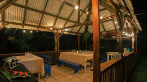 An outdoor covered dining area with tables and benches, string lights, and a wooden railing. - Boca Tapada Lodge (Pital)