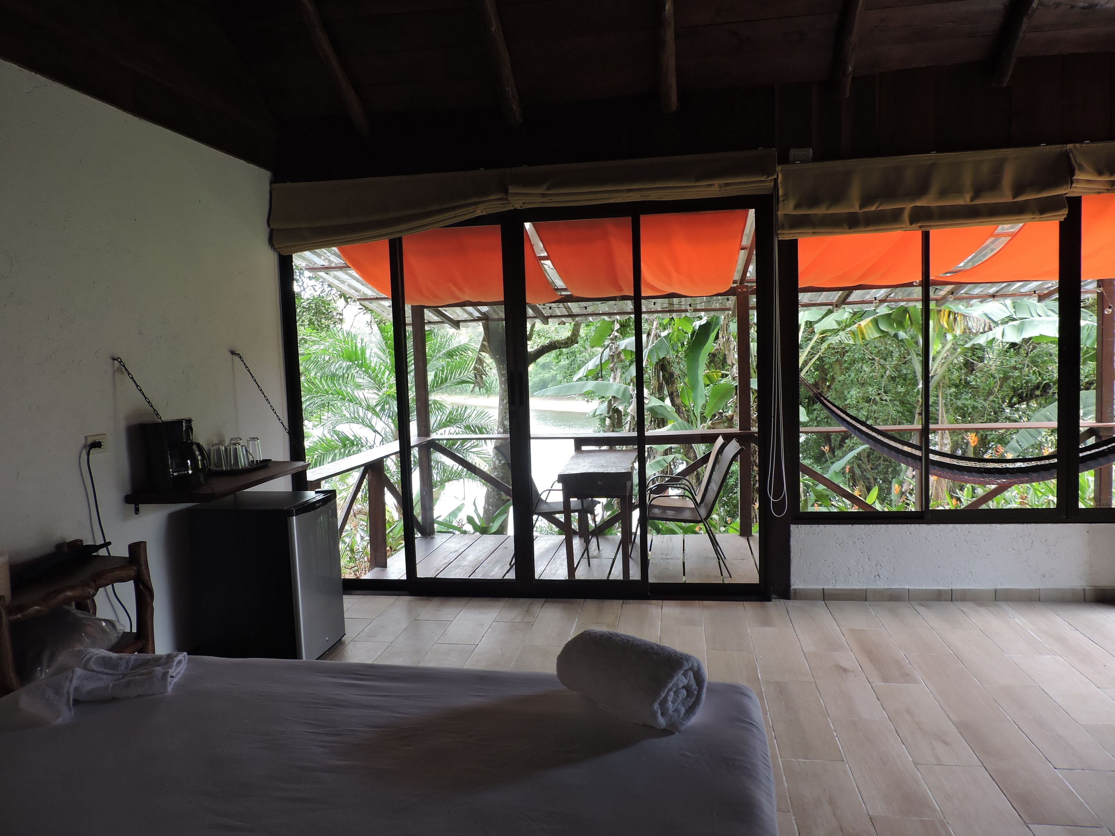 A hotel room with a bed, a desk, and a view of a lush garden through large windows.