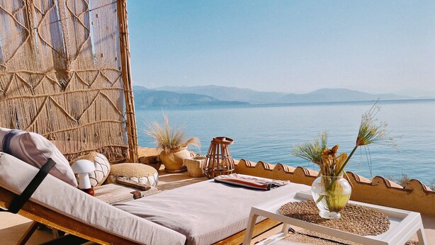 A sun lounger with a cushion, a small table with a vase, and a view of the sea and mountains.