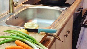 A kitchen with a stainless steel sink, wooden cabinets, a pot on the stove, and vegetables on the counter.