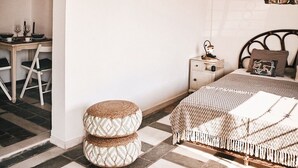 A cozy bedroom with a bed, a small bedside table, a wall-mounted TV, and a dining area with chairs and a table.