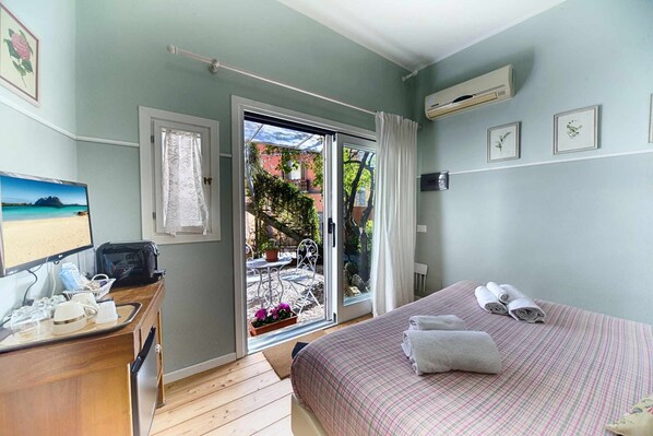 A bedroom with a bed, a desk with a computer and a tray of items, a window with curtains, and a view of the outside. - Garden Room Casa Satta Olbia City Center (Olbia)