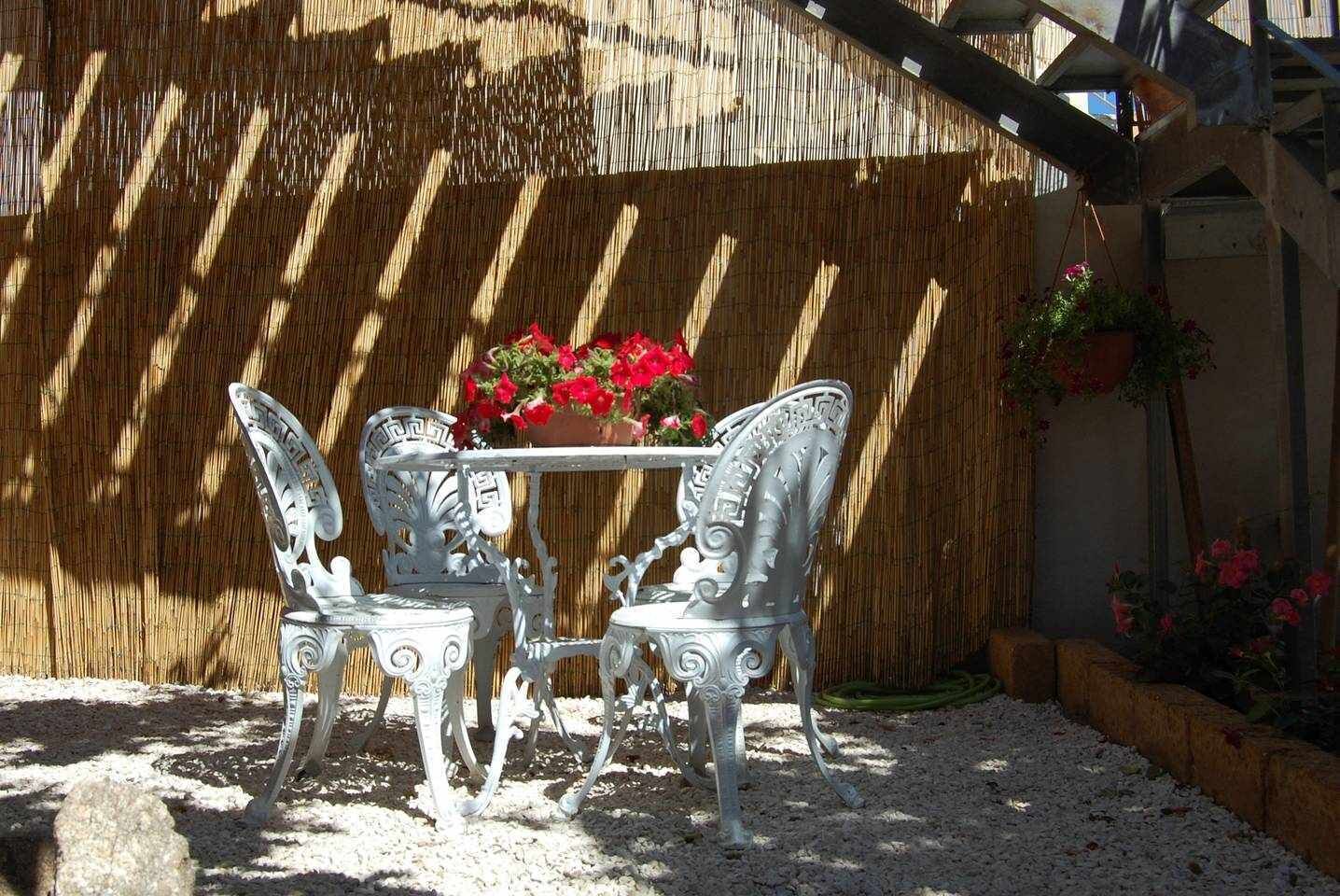 A patio with a table and chairs, a bamboo fence, and potted plants.