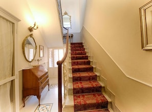 Eine Treppe mit roten Teppichstufen, eine Holzkommode und ein Spiegel an der linken Wand.