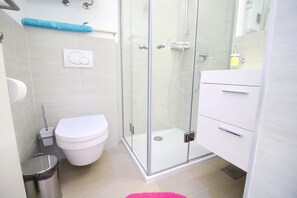 Une salle de bain moderne avec une douche à parois de verre, des toilettes blanches et un lavabo blanc avec un miroir.