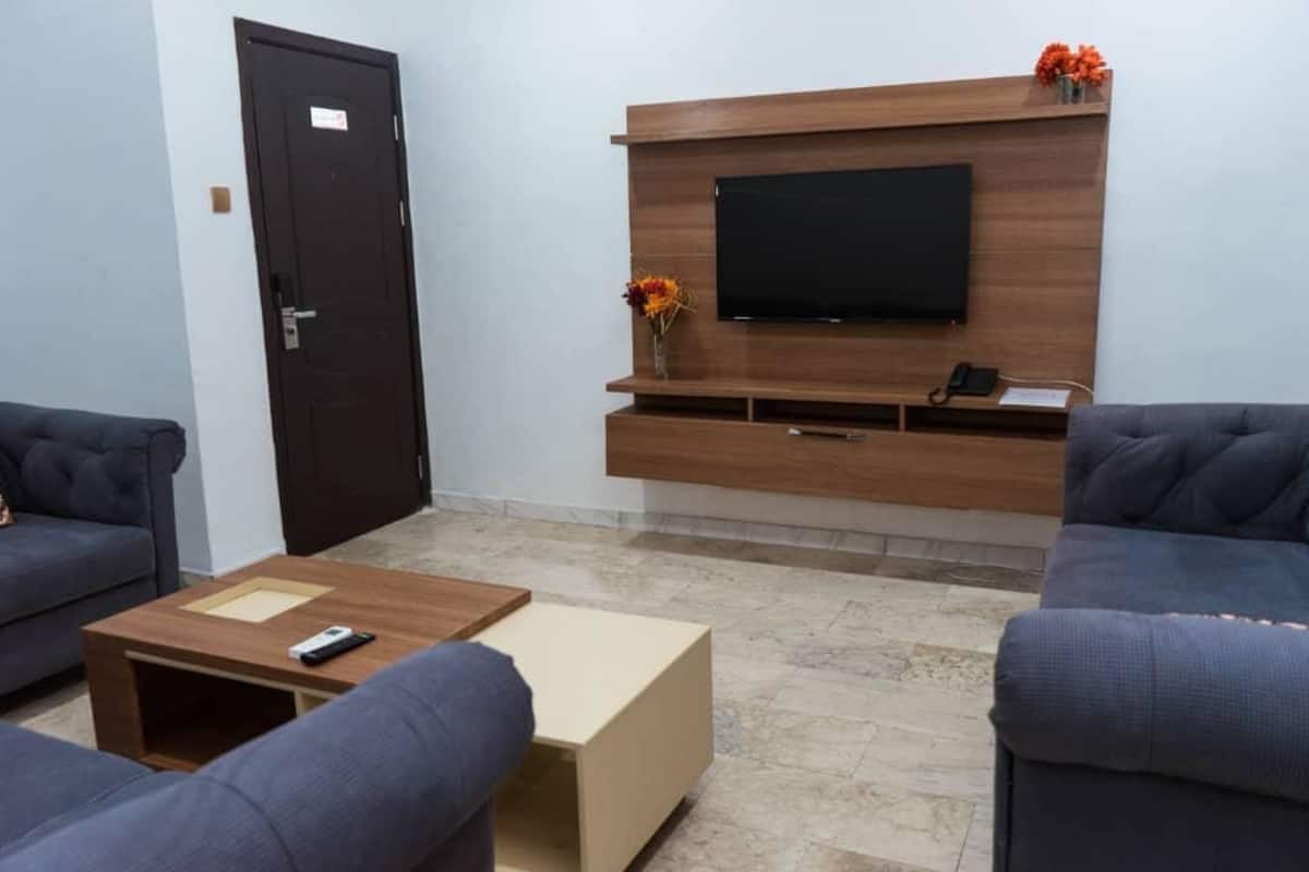 Un saló modern amb dos sofàs, una taula de centre, un televisor fixat a una paret de fusta i una porta.
