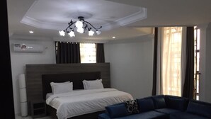 A modern hotel room with a large bed, a blue sofa, and a wooden coffee table. - SS3 Boutique Hotel (Port Harcourt)