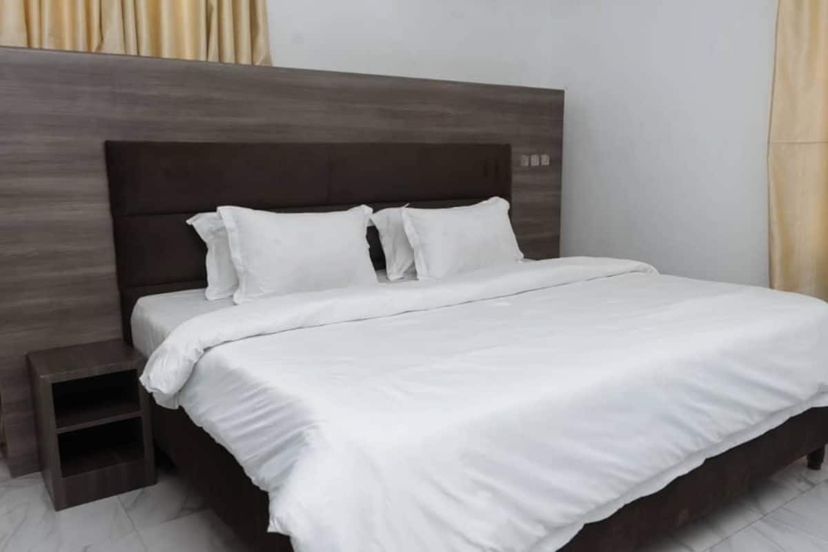 Un llit ben fet amb roba de llit blanca i un capçal fosc en una habitació d'hotel.