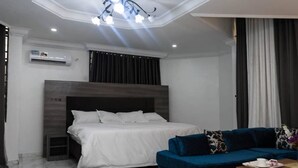 A modern bedroom with a large bed, a blue sofa, and a small table with a tray. - SS3 Boutique Hotel (Port Harcourt)