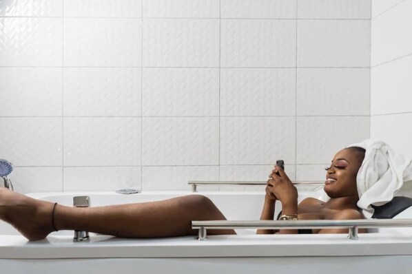 A person lying in a bathtub with a towel on their head, holding a smartphone.