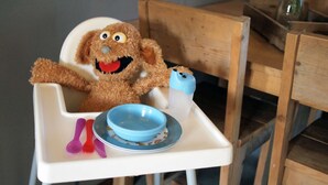 A high chair with a plush toy and a blue bowl.