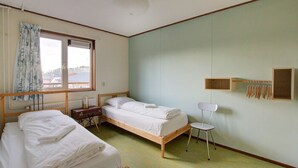 A room with two wooden beds, a small desk, a chair, and a window with curtains.