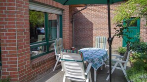 Un patio con una mesa, sillas, un paraguas verde y un muro de ladrillo.