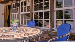 Een ronde tafel met een mozaïekblad, twee blauwe stoelen en een potplant.