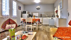 A modern kitchen with white cabinets, a microwave, and a coffee maker. There is a dining area with a table, chairs, and a colorful chair. - Cottage of Suzette ---- (LA FORET-FOUESNANT)