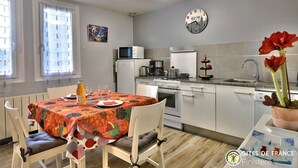 A modern kitchen with white cabinets, a microwave, a coffee maker, and a sink. There is a dining table with a colorful tablecloth and chairs. - Cottage of Suzette ---- (LA FORET-FOUESNANT)