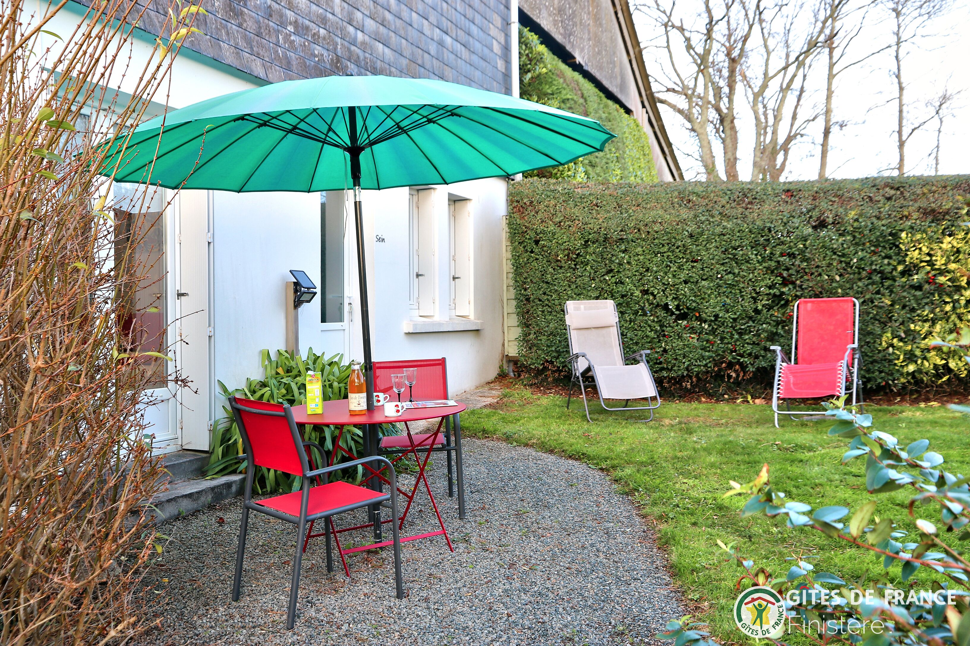 Eine Terrasse mit Tisch und Stühlen, einem grünen Sonnenschirm und einem roten Stuhl.