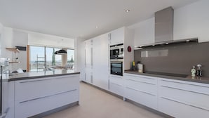 A modern kitchen with white cabinetry, a large island, and a view through the window.