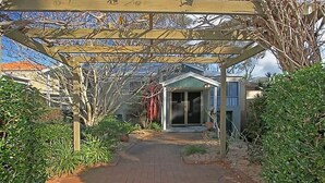 Un chemin menant à une maison surmontée d’une pergola en bois.