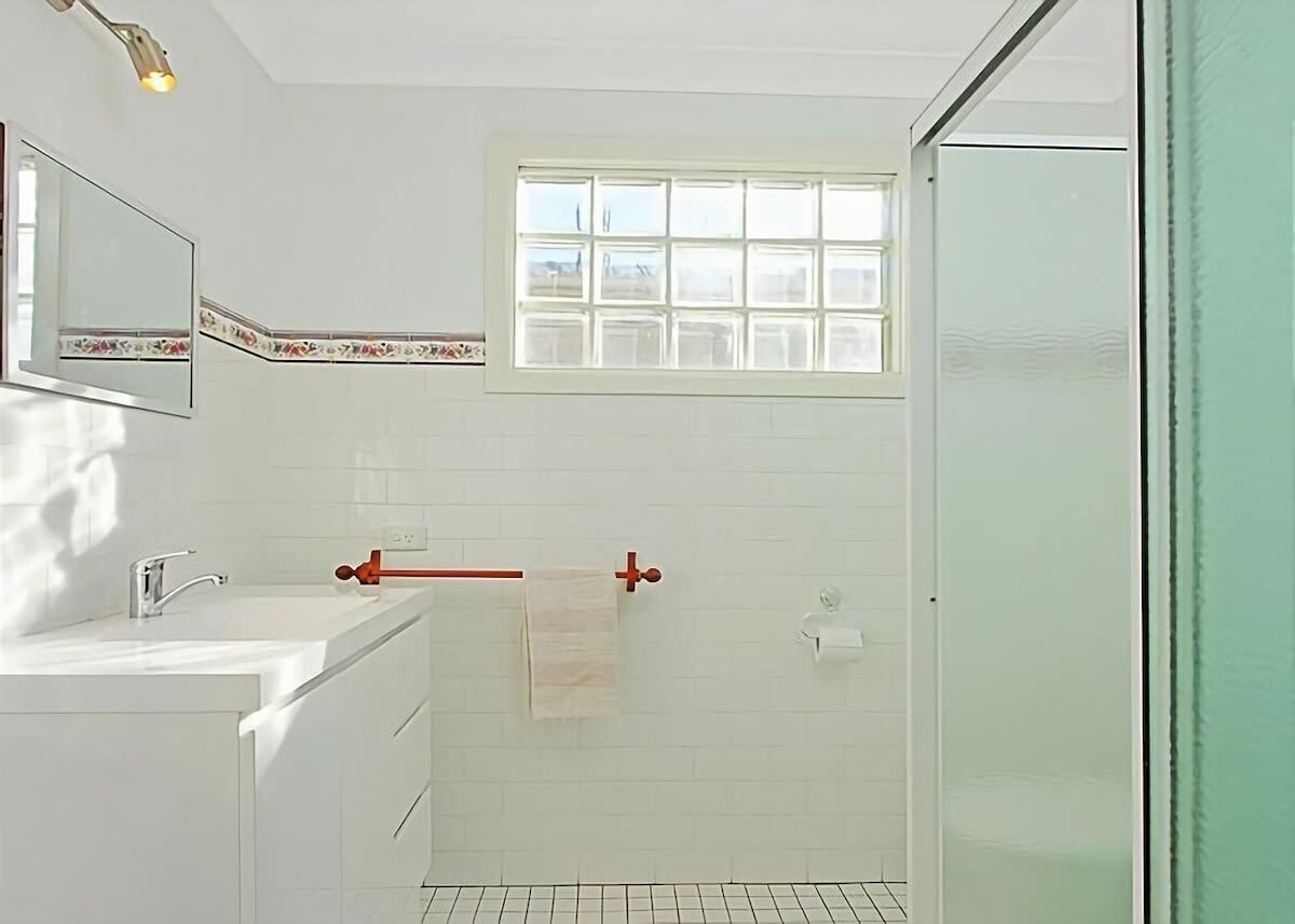 Een badkamer met een wit wastafelmeubel, spiegel en raam.