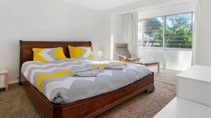 Une chambre moderne avec un lit en bois, un ventilateur de plafond, une grande fenêtre donnant sur un beau paysage, une chaise et une petite table.