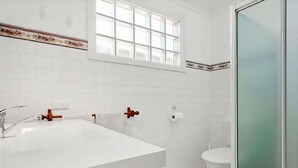Une salle de bain avec un lavabo, des toilettes et une douche, le tout de couleur blanche.