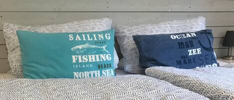 A bed with patterned bedding and two pillows with nautical-themed text.