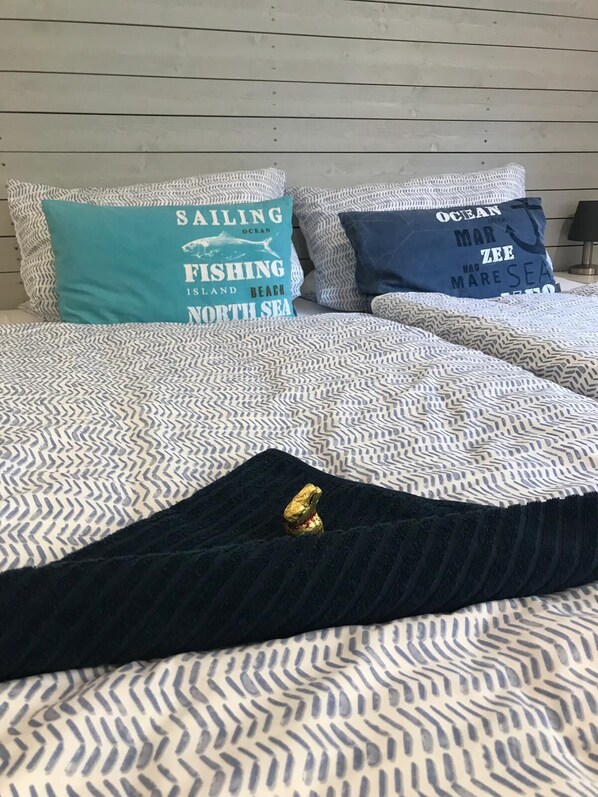 A bed with patterned bedding and two pillows with nautical-themed text. - Dock 8 beaches: Only 50 meters to the sandy beach and the promenade (Strande)