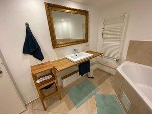 A bathroom with a wooden vanity, a white sink, a mirror with a gold frame, a bathtub, and a window with blinds. - Dock 8 beaches: Only 50 meters to the sandy beach and the promenade (Strande)