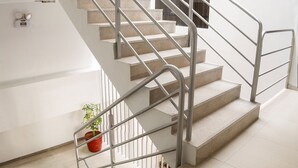 Eine moderne Treppe mit Metallgeländern und beigefarbenen Stufen, die zu einer Empfangsebene mit einem Blumentopf führt.