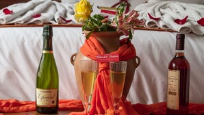 Ein Tisch mit zwei Weinflaschen und zwei Weingläsern, eine Vase mit einer gelben Rose und ein weißes Tuch mit Rosenblüten.