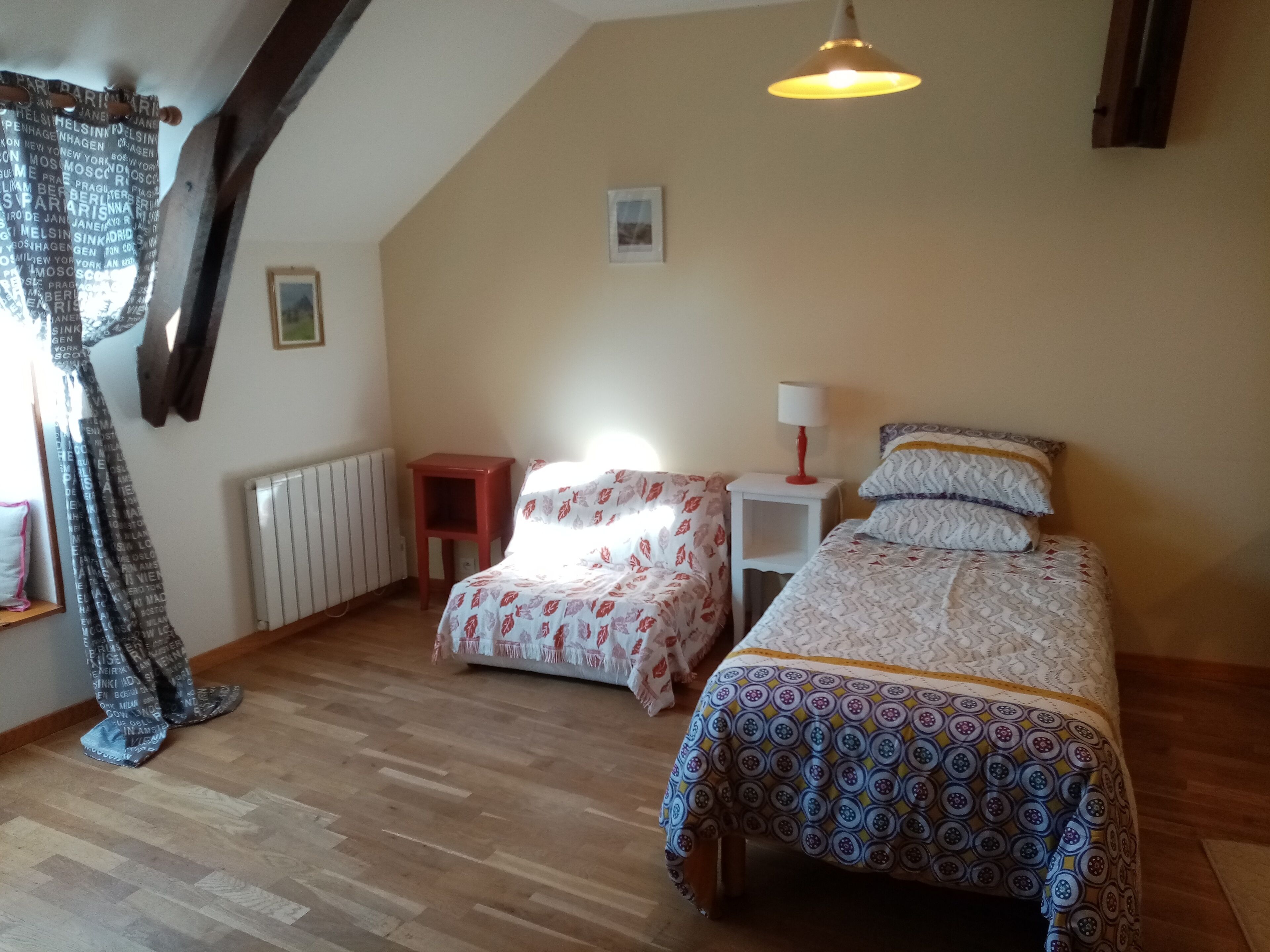 Ein Schlafzimmer mit zwei Betten, einem roten Nachttisch, einem weißen Beistelltisch, einer Hängelampe und einer Heizung.