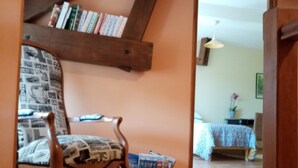 Um quarto acolhedor com teto de madeira, uma poltrona estampada, um tapete pequeno e uma estante cheia de livros.