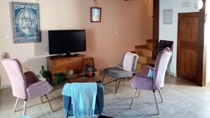 Uma sala de estar com televisão, duas cadeiras, uma mesa pequena e uma escada que leva a outro cômodo.