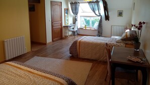 Quarto com duas camas, uma escrivaninha, uma cadeira, um radiador e uma janela com cortinas.