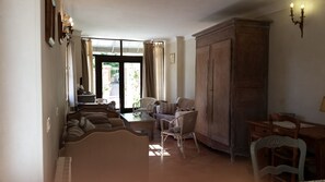 Amplia sala de estar con un conjunto de sofás, una mesa de comedor y sillas. Hay un gran armario de madera y una vista al exterior a través de un ventanal.