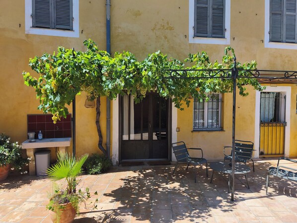 A courtyard with a pergola covered in grapevines, a tiled patio, and outdoor seating.