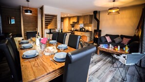 A modern dining area with a wooden table set for six, black chairs, and a kitchen in the background. - The mountain with family or friends ... the cottage "Huski" is for you! (Valloire)