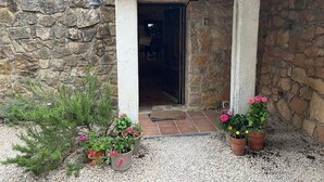 A stone building with a tiled entrance and a wooden overhang. There are potted plants with flowers in front of the entrance.