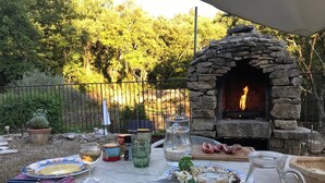 An outdoor dining area with a stone oven, plates, cutlery, and a pitcher of drink.