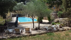 A swimming pool surrounded by a stone wall, with a wooden deck and lounge chairs.