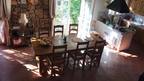 A rustic kitchen with a stone wall, wooden beams, and a dining area with a table and chairs.