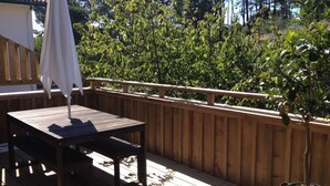 Une terrasse en bois avec une table et un parasol, entourée d’une clôture en bois et d’une végétation luxuriante.