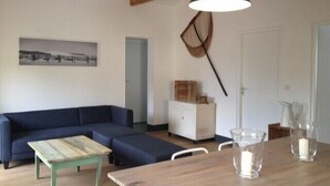 Un salon avec un canapé bleu, une table basse en bois, un meuble blanc et une lampe suspendue.