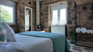 Ein Schlafzimmer mit Steinwand, einem Bett mit grüner Decke, einem Spiegel und einem Regal mit gerollten Handtüchern.