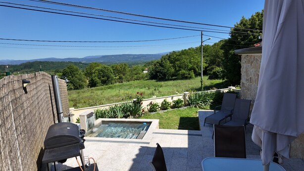 Eine Terrasse mit Grill, kleinem Pool und Blick auf eine grüne Landschaft mit Hügeln.